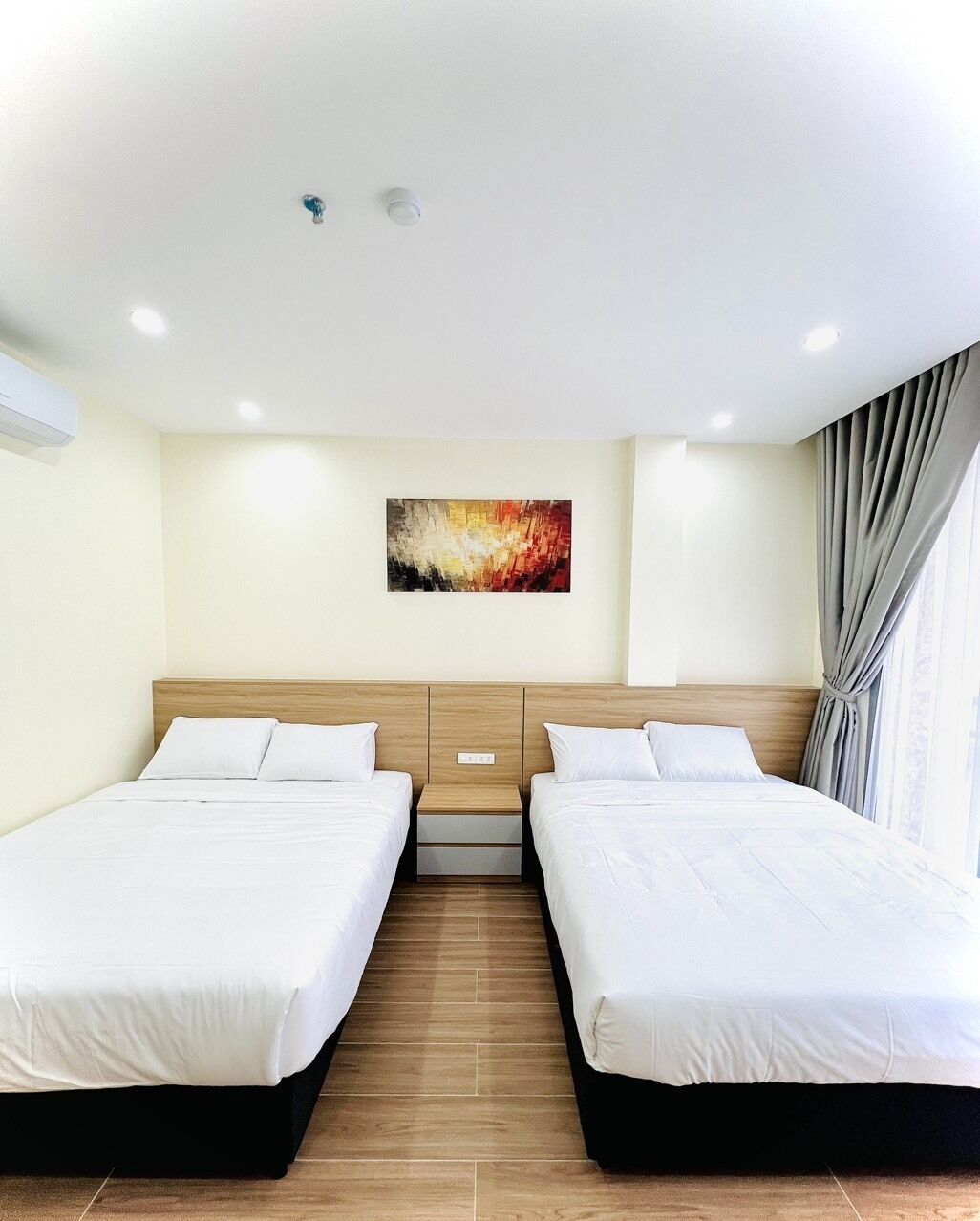 Habitación de hotel con dos camas, cabecera de madera, un cuadro en la pared y una ventana con cortinas.