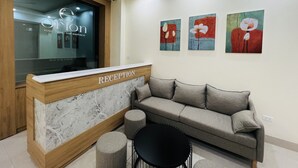 A reception area with a marble reception desk, a grey sofa, and three abstract floral paintings on the wall. - Orion Hotel Halong (Hong Gai)