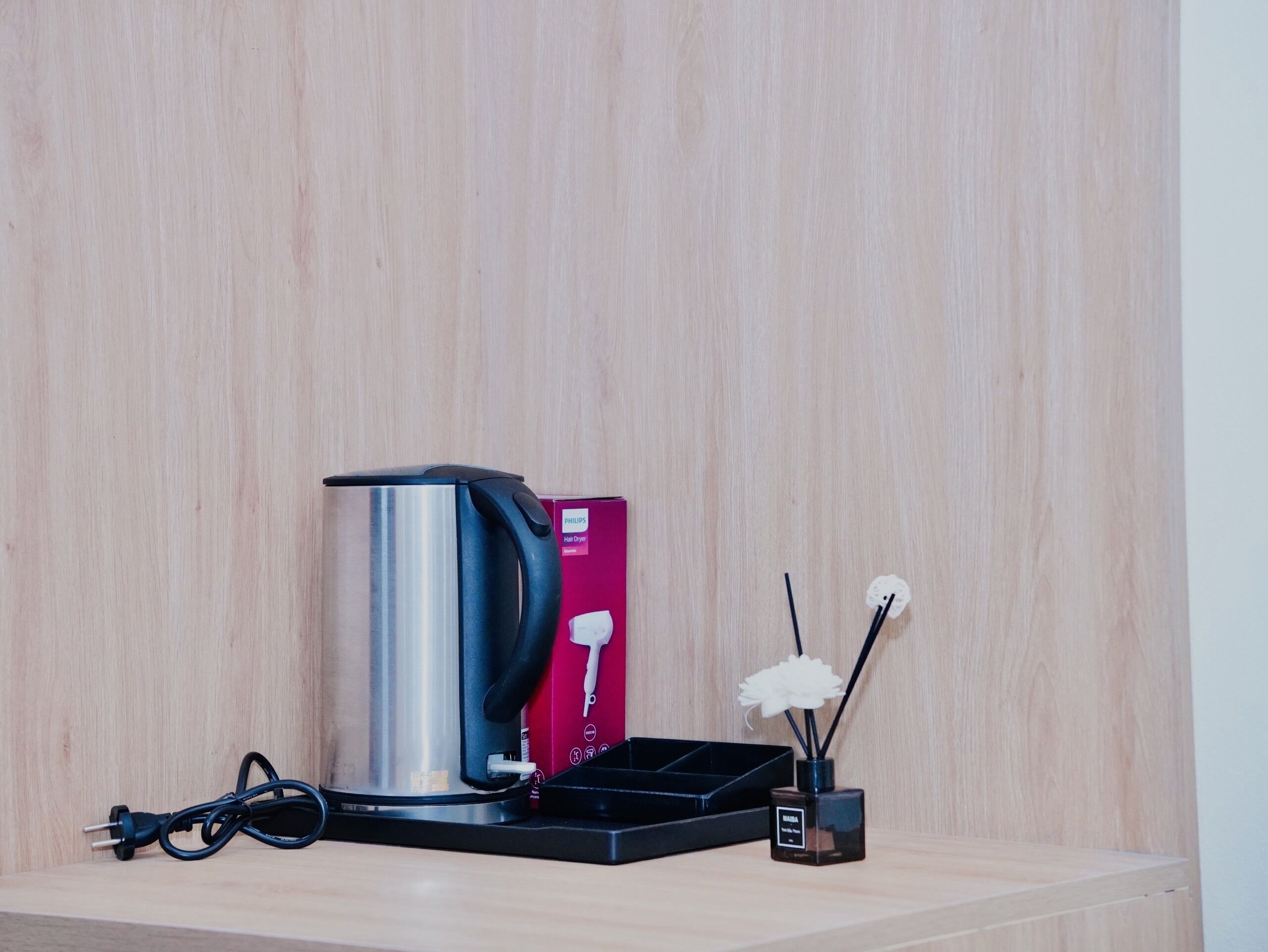 A hair dryer on a wooden surface with a box and a bottle of perfume.