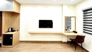 A modern, minimalist room with a built-in TV, a small desk, a chair, and a window with blinds. - Orion Hotel Halong (Hong Gai)