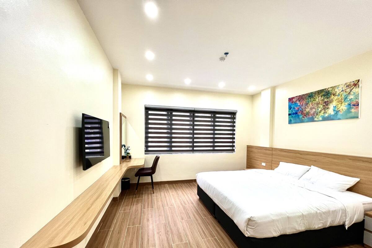 Une chambre d’hôtel équipée d’un lit, d’un bureau, d’une chaise, d’une télévision et d’une fenêtre avec des stores.