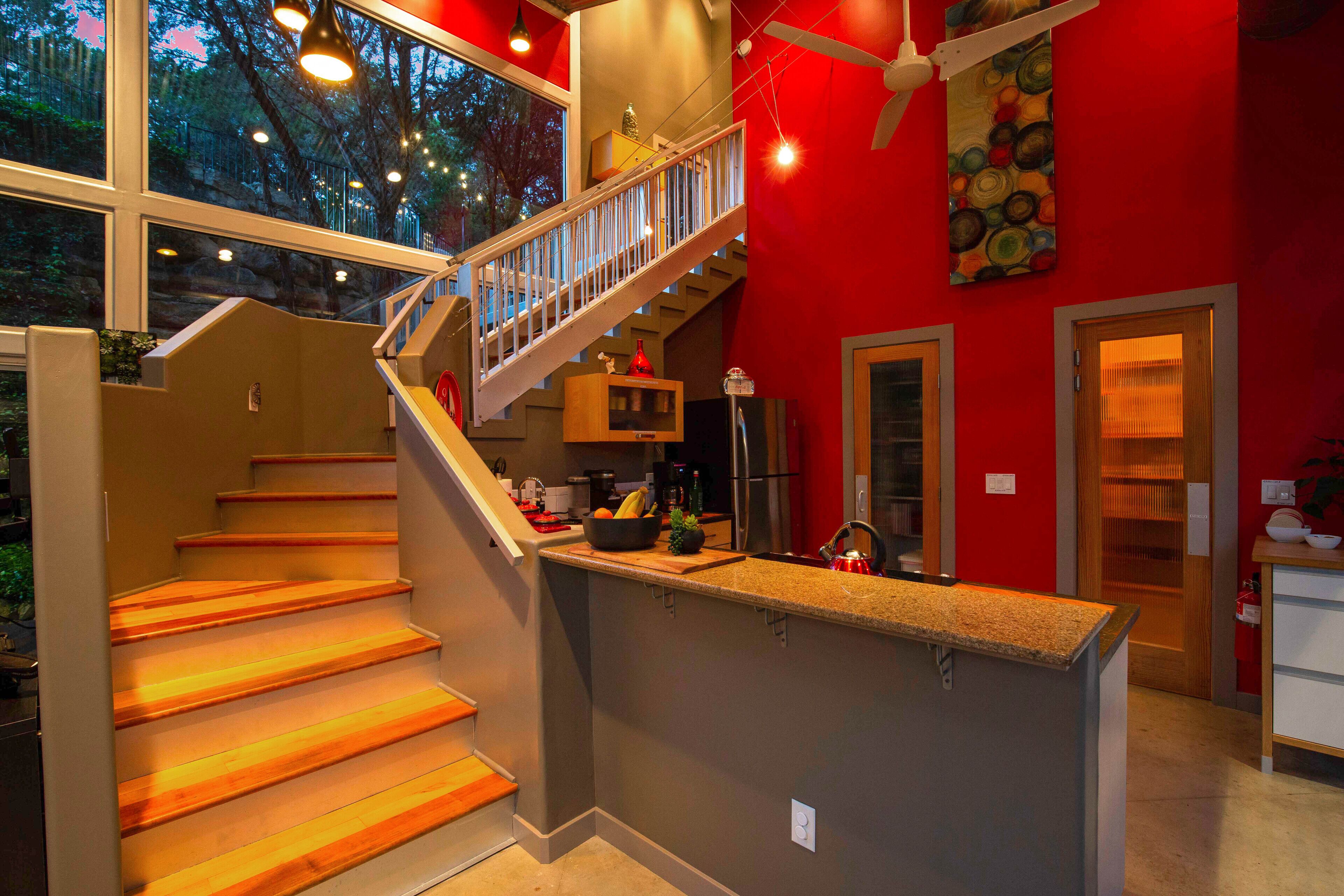 A modern kitchen with a wooden staircase, a kitchen island, and a red accent wall.