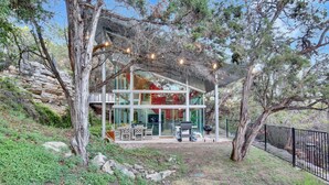 Uma casa moderna com fachada de vidro, área de estar externa e um muro de contenção de pedra.