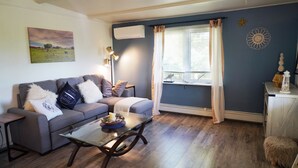 A living room with a sofa, coffee table, and a window with curtains. - Cozy private cottage with picturesque scenery (New Glasgow)