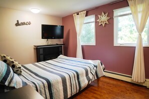 A bedroom with a bed, a TV, a window with curtains, and a wall decoration. - Cozy private cottage with picturesque scenery (New Glasgow)