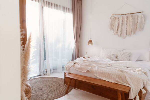 A bedroom with a wooden bed, white bedding, a woven rug, and a hanging light fixture.