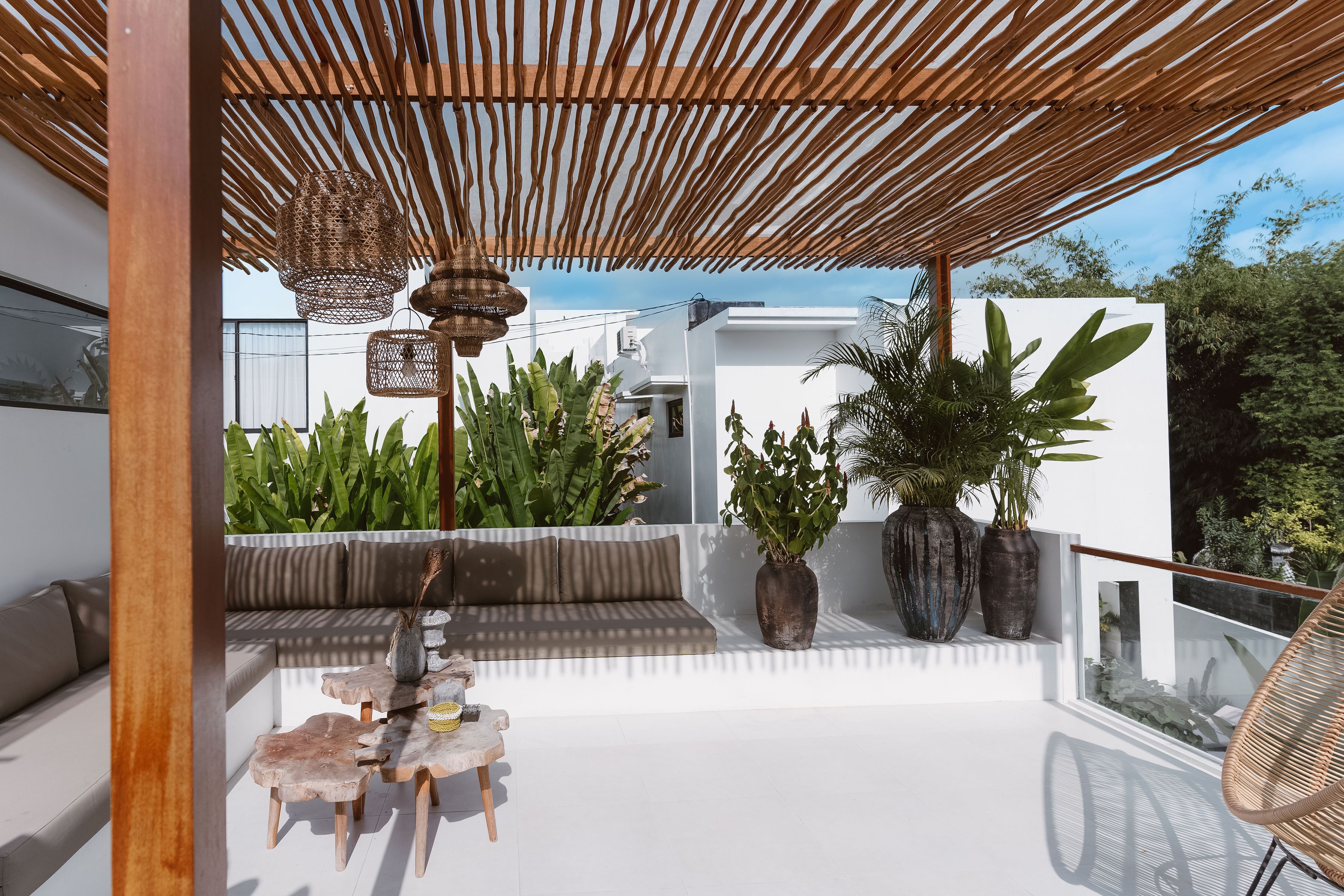 A modern outdoor seating area with a wooden pergola, a cushioned bench, and a table with chairs.