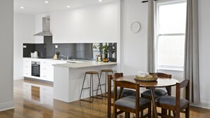 A modern kitchen with white cabinets, a central island with stools, and a dining area with a round table and chairs. - North Edge Cottage ~ Free Parking, City, Warm (Launceston)