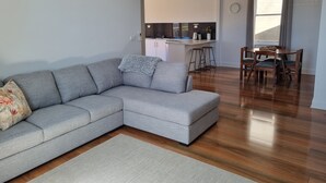 A modern living room with a grey sectional sofa, a small rug, and a wooden dining table with chairs. - North Edge Cottage ~ Free Parking, City, Warm (Launceston)