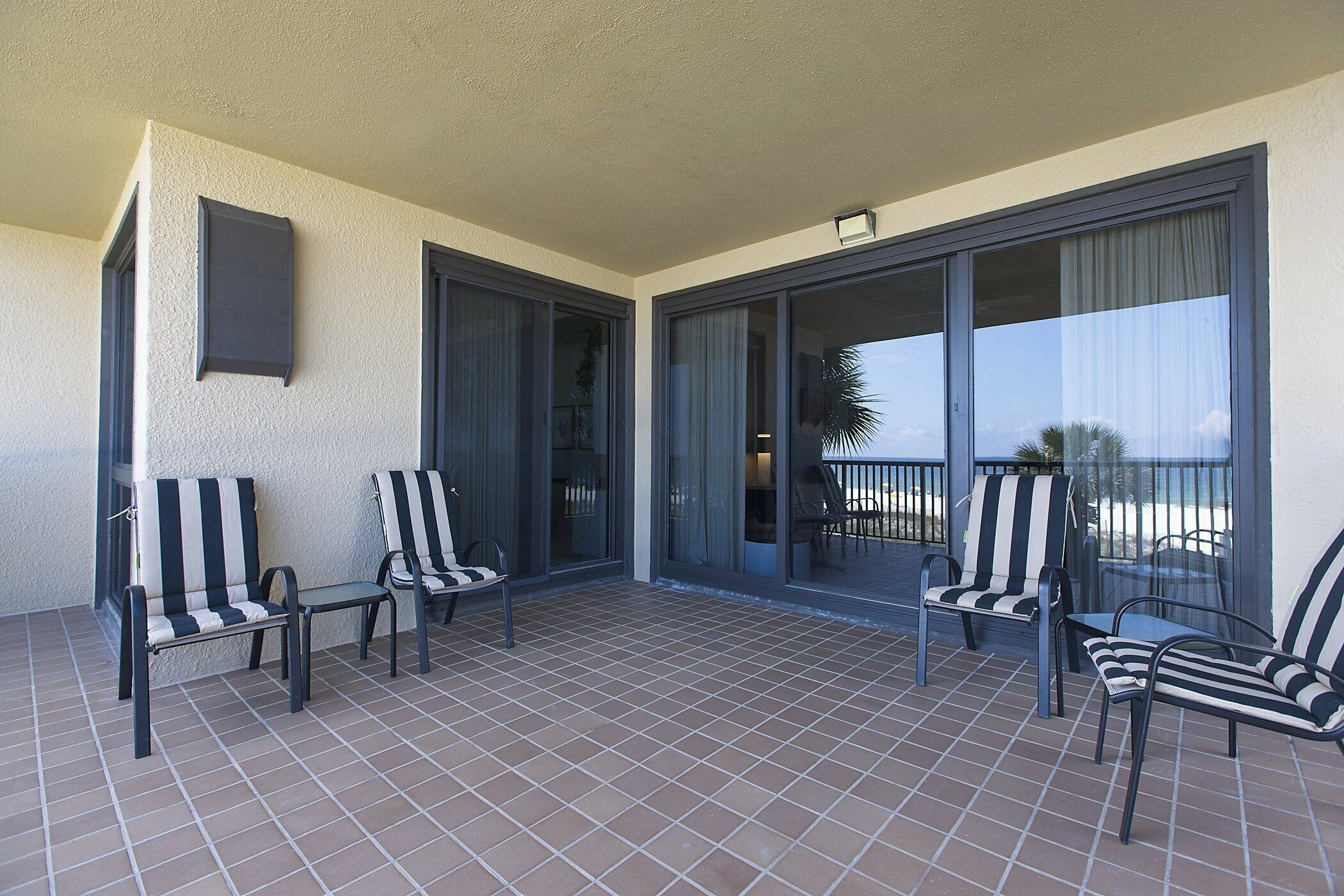 Ein Balkon mit vier gestreiften Stühlen und einem Tisch, großen Schiebeg lass-Türen und Blick auf den Strand.
