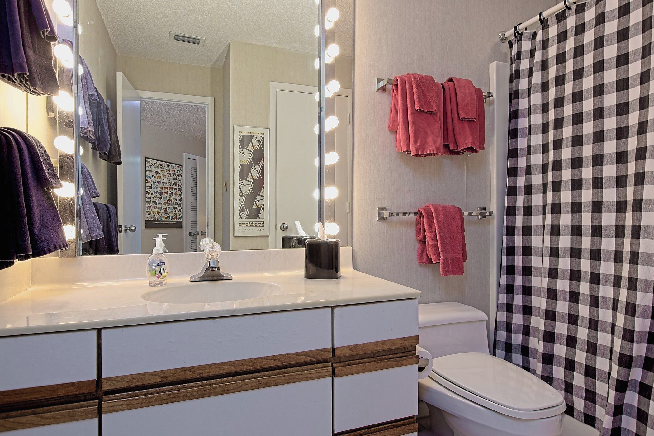 A bathroom with a vanity, mirror, lights, and towels.