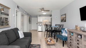 A modern living room with a gray sofa, a coffee table with decorative items, a dining area with chairs and a table, and a kitchen in the background. - Beachfront Getaway at Gulf Shores Plantation! (Gulf Shores)