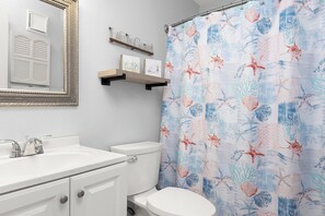 Un baño con lavamanos blanco, inodoro y cortina de ducha con motivos marinos.