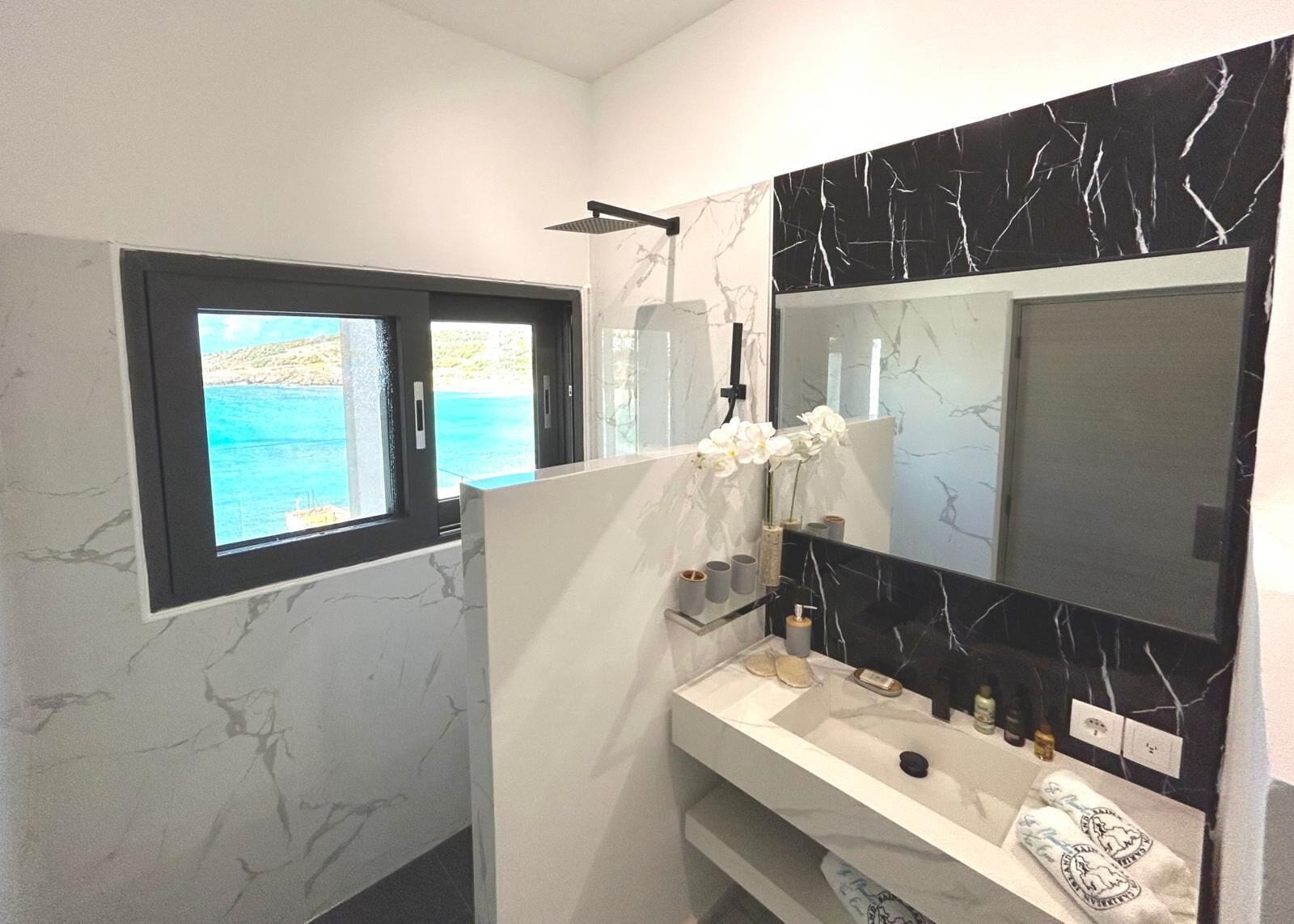Un bagno con un grande specchio, una finestra vista mare e un piano di lavoro in marmo.
