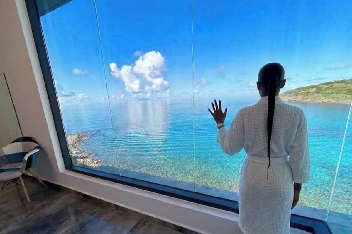 A person standing by a large window with a view of a body of water and a distant shoreline.