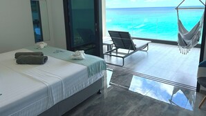 Een hotelkamer met een bed, een stoel, een hangmat en uitzicht op de oceaan.