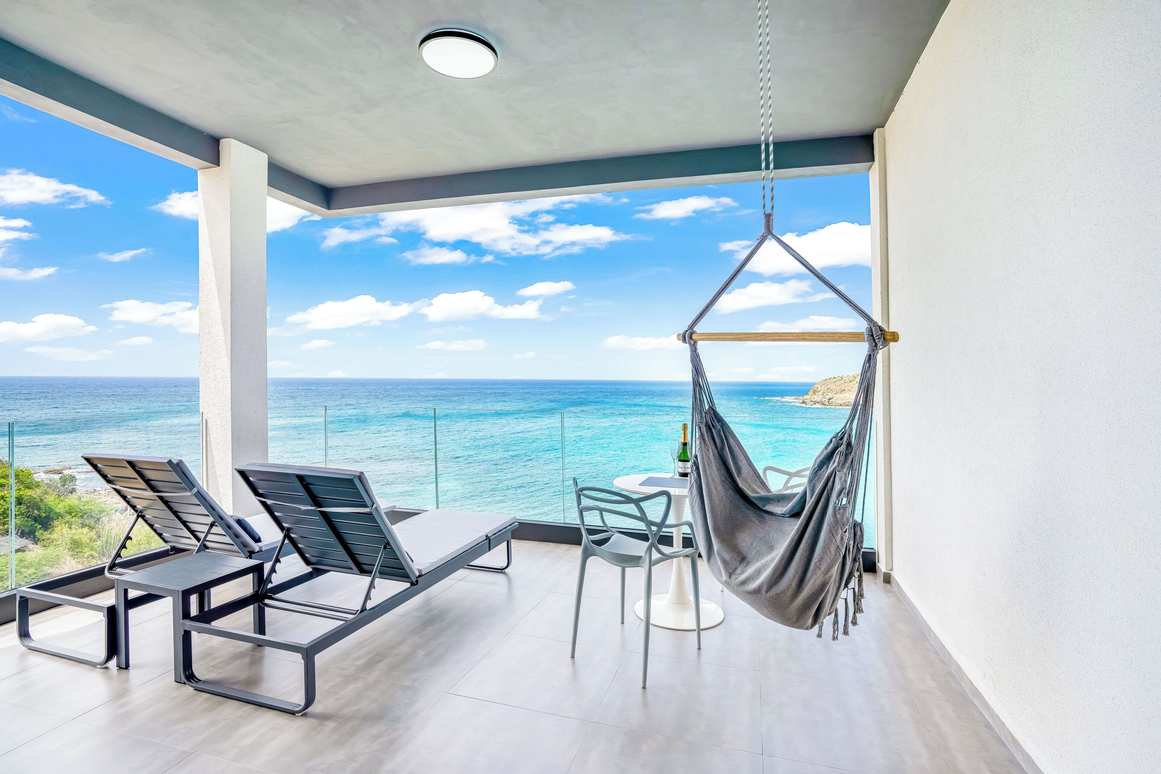 A balcony with a view of the ocean, a hammock, and two lounge chairs.