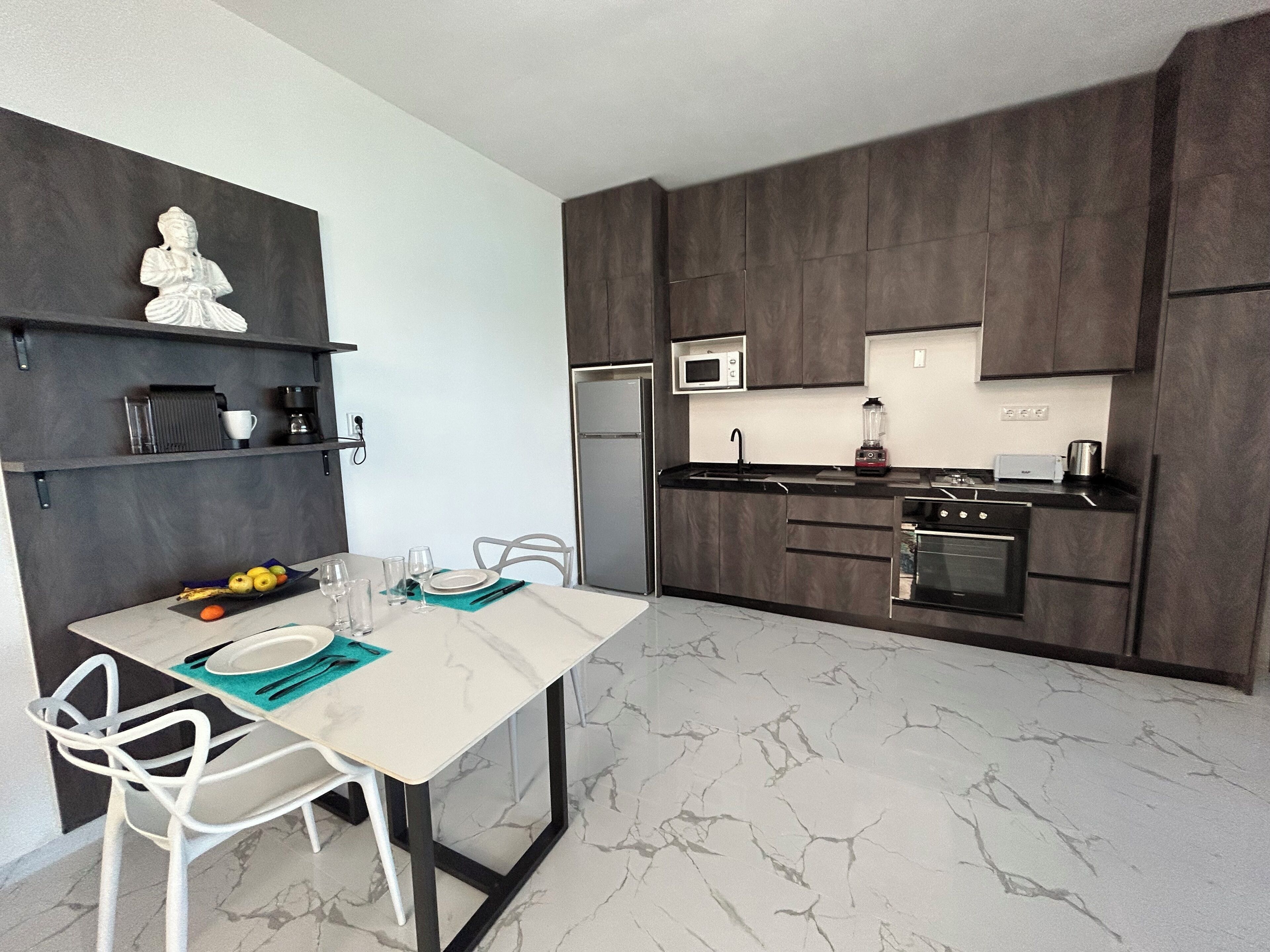 Eine moderne Küche mit dunklen Holzschränken, einer weißen Marmorarbeitsplatte und einem Essbereich mit weißen Stühlen und einem weißen Tisch.