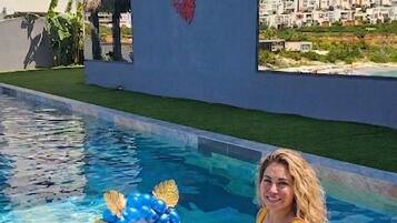 A pool with clear water, a woman in a yellow swimsuit, and a decorative basket with balloons.