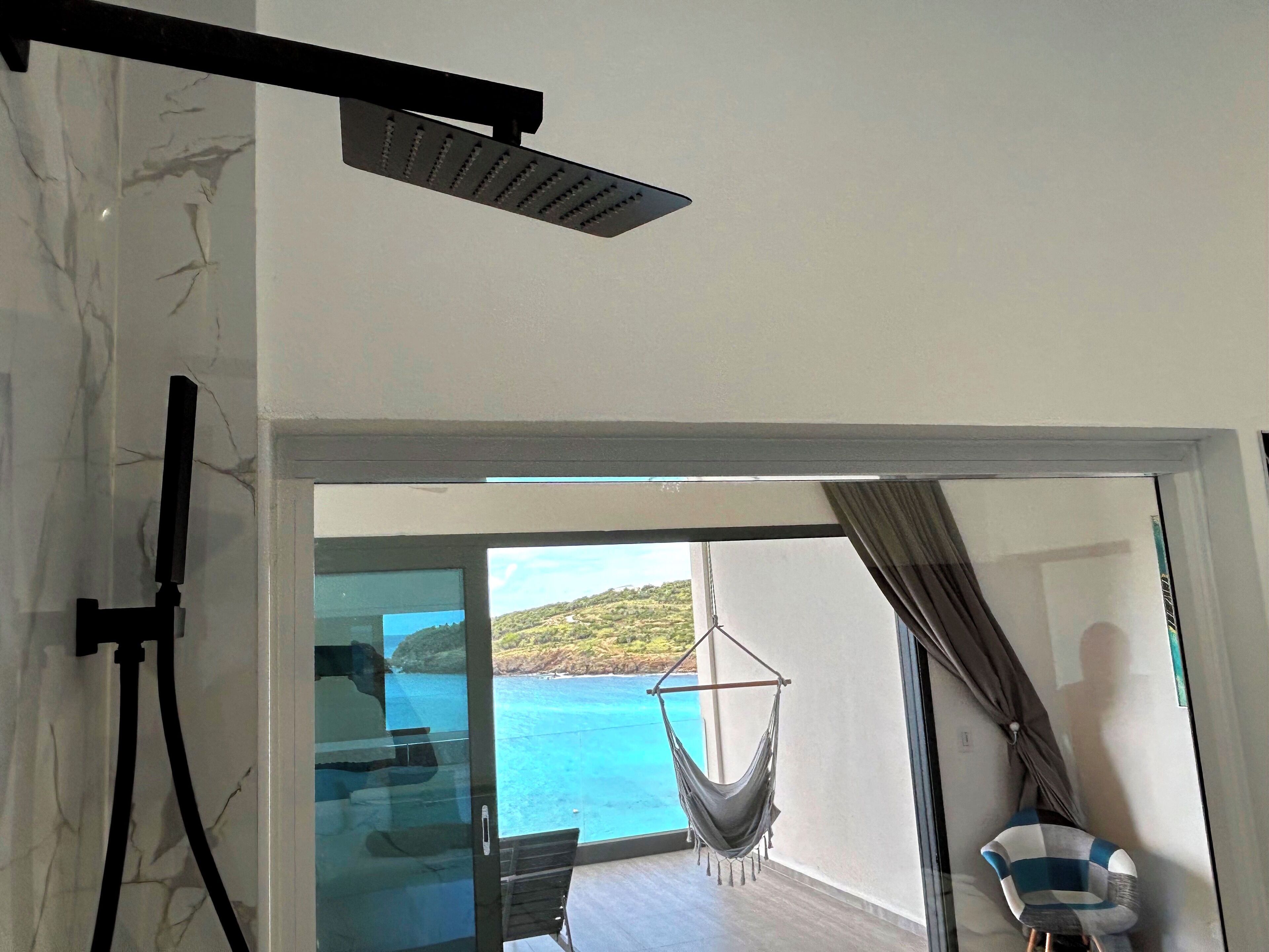 Une pièce dotée d’une porte vitrée donnant sur un balcon avec vue sur la mer et un hamac.