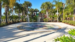 Un espace paysager agrémenté d’un bassin circulaire, de palmiers et d’une structure de jeux pour enfants.