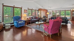 A spacious living room with hardwood floors, a ceiling fan, and large windows offering a view of greenery outside. - Duskin Point Retreat - near Duskin Point Marina (Jasper)