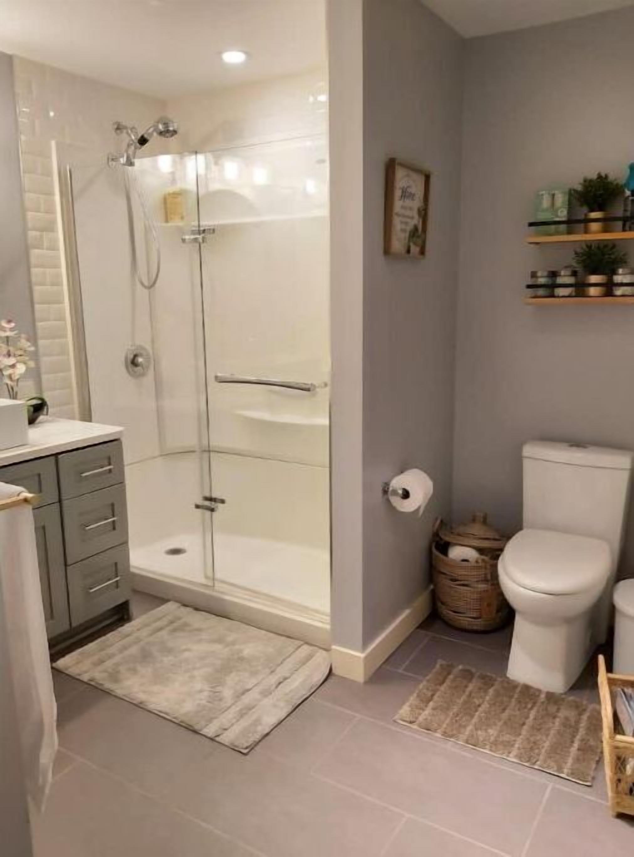Une salle de bain moderne dotée d’une douche à parois de verre, de toilettes, d’un lavabo avec un meuble-vasque et d’une petite étagère ornée d’objets décoratifs.