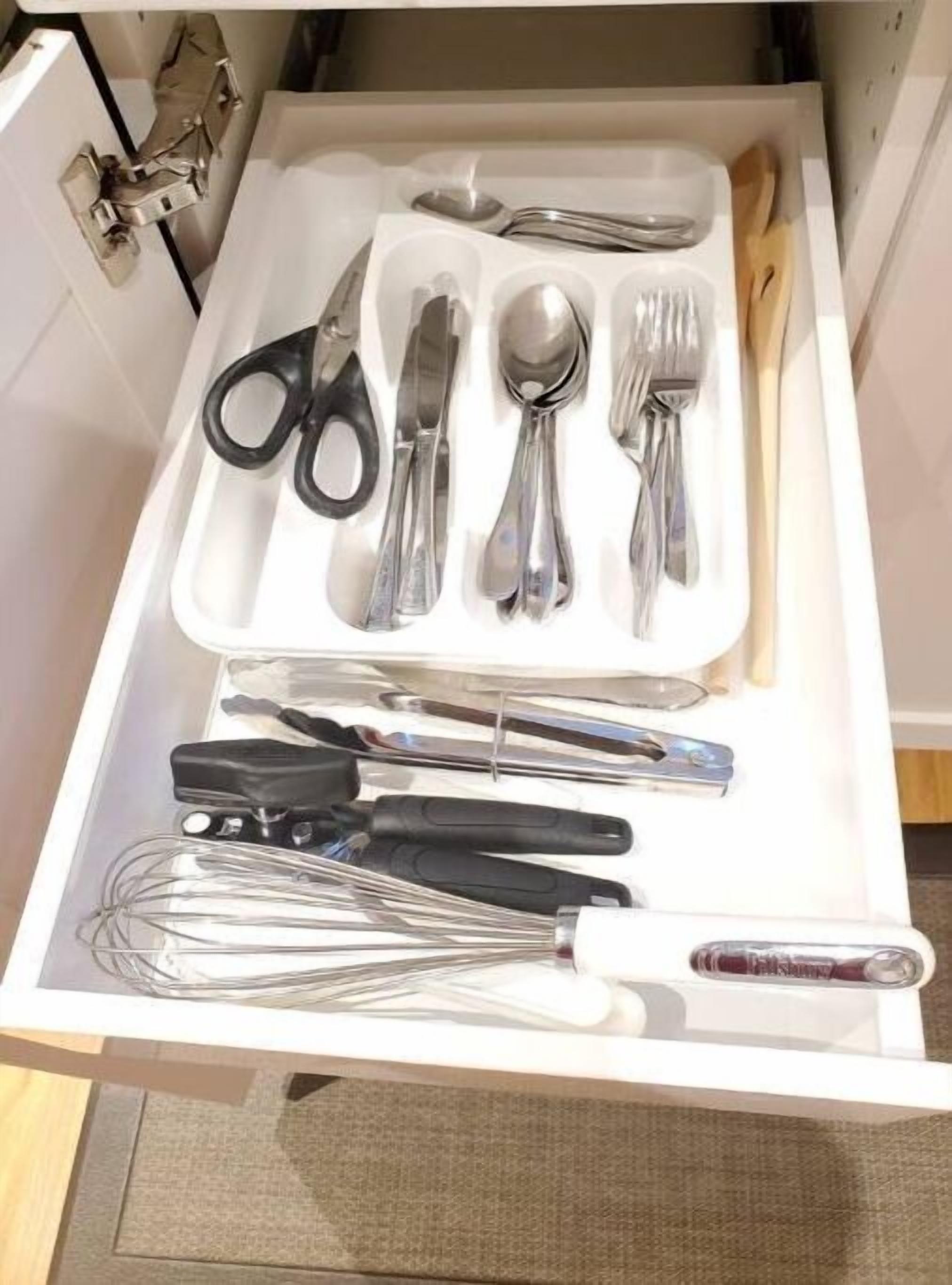 A drawer containing various kitchen utensils including scissors, knives, spoons, forks, and whisks.