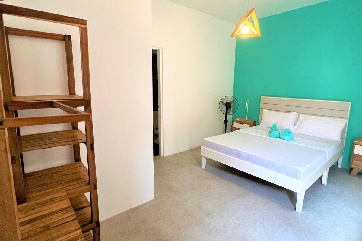 A bedroom with a bed, a wooden shelf unit, a nightstand, and a hanging light fixture.