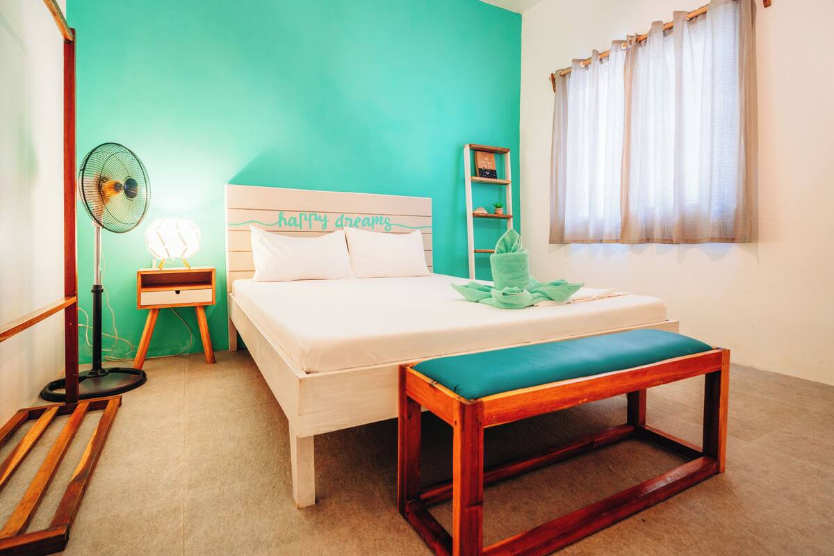 A bedroom with a bed, bedside table, nightstand, lamp, and a wooden bench.