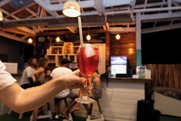 A person holding a glass with a straw in a bar setting.