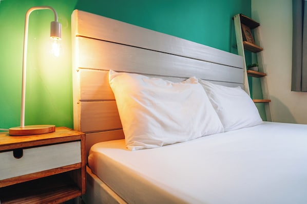 A neatly made bed with white linens, a wooden headboard, and a bedside lamp. - My Green Hostel (San Vicente)