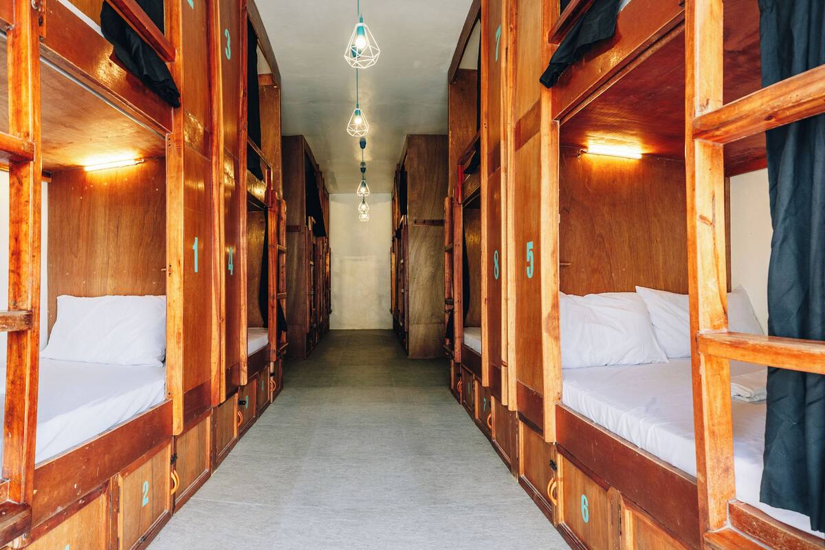 A corridor with wooden bunk beds, numbered doors, and a hanging light fixture.