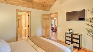 Un dormitorio con cama, techo de madera, televisión, mesita de noche y puerta que da a otra habitación.
