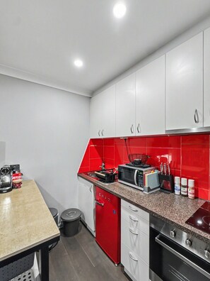 A modern kitchen with white cabinets, a red backsplash, and stainless steel appliances including a microwave, stove, and dishwasher. - A Cool Little Hideaway in the Heart of Fitzroy (Fitzroy)