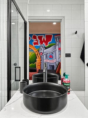 A modern bathroom with a large black sink, a glass shower enclosure, and a colorful mural on the wall.