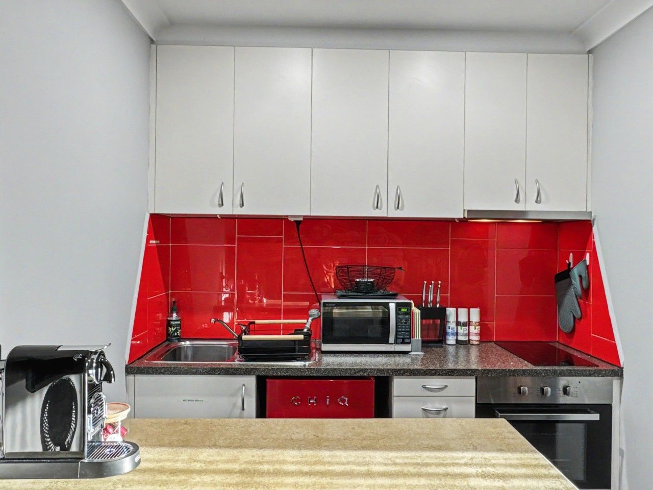 A kitchen with white cabinets, a red backsplash, a microwave, a toaster, and a coffee maker.