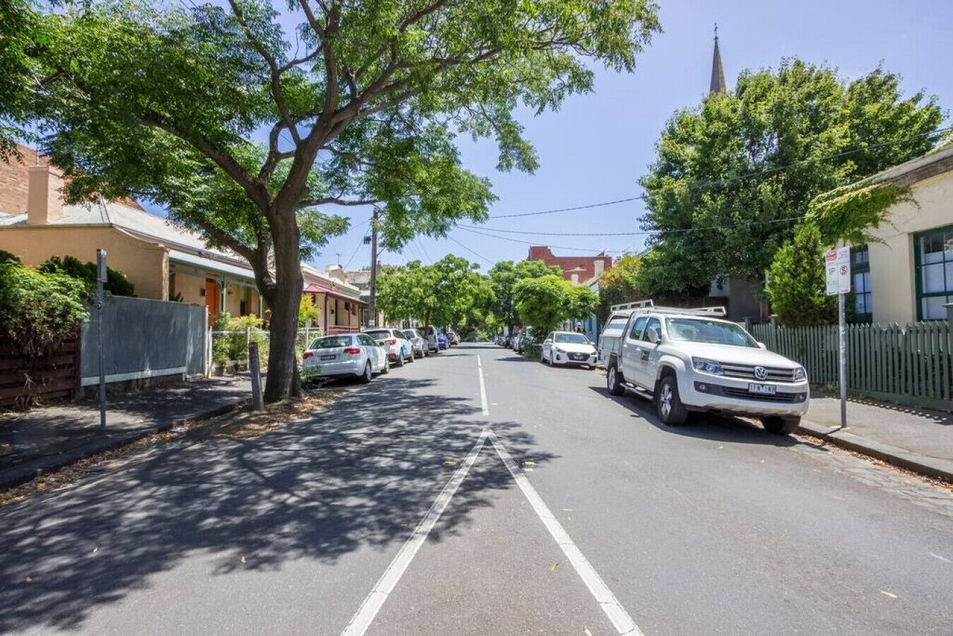 A street lined with parked cars and trees, with buildings on either side.