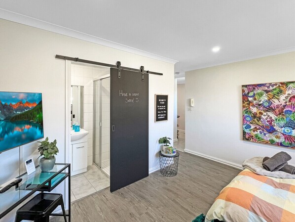 A modern bedroom with a bed, a desk with a computer, a TV, and a door with a sign.