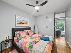 A bedroom with a bed, a ceiling fan, a bedside table, and a door leading to a balcony.