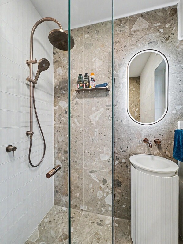 A bathroom with a glass-enclosed shower, a white sink, and a mirror.