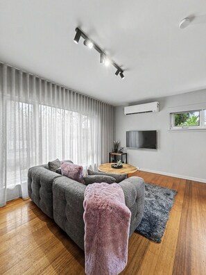 A modern living room with a grey sofa, a round coffee table, and a flat-screen TV mounted on the wall. - Ground floor one bedroom apartment in South Yarra (South Yarra)