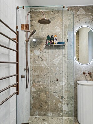 A modern bathroom with a glass-enclosed shower, a white sink, and a marble-tiled wall.