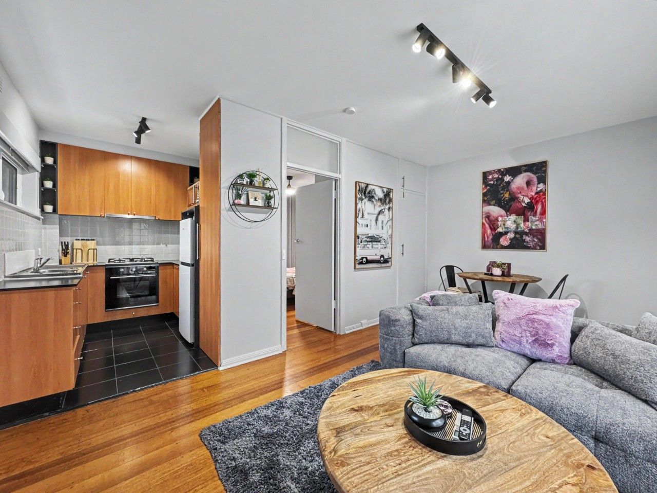 A modern kitchen with wooden cabinets, a built-in oven, and a dining area with a grey sofa and a coffee table.