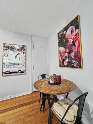 A dining area with a round wooden table, black chairs, and two framed artworks on the wall.