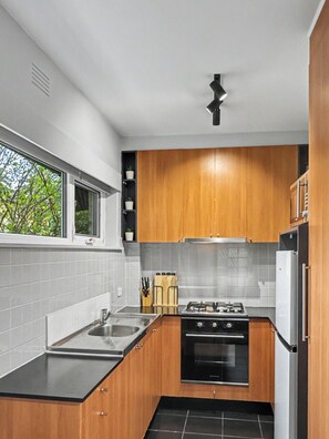 A modern kitchen with wooden cabinets, a gas stove, a sink, and a window. - Ground floor one bedroom apartment in South Yarra (South Yarra)