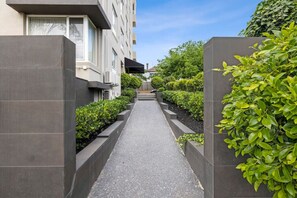 A narrow pathway flanked by buildings and greenery, leading to a central structure.