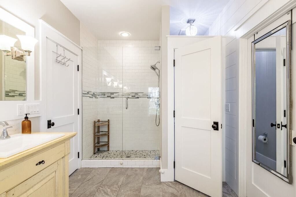 A bathroom with a white vanity, a glass shower enclosure, and a white door.