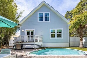 A light blue house with a white porch and a swimming pool.