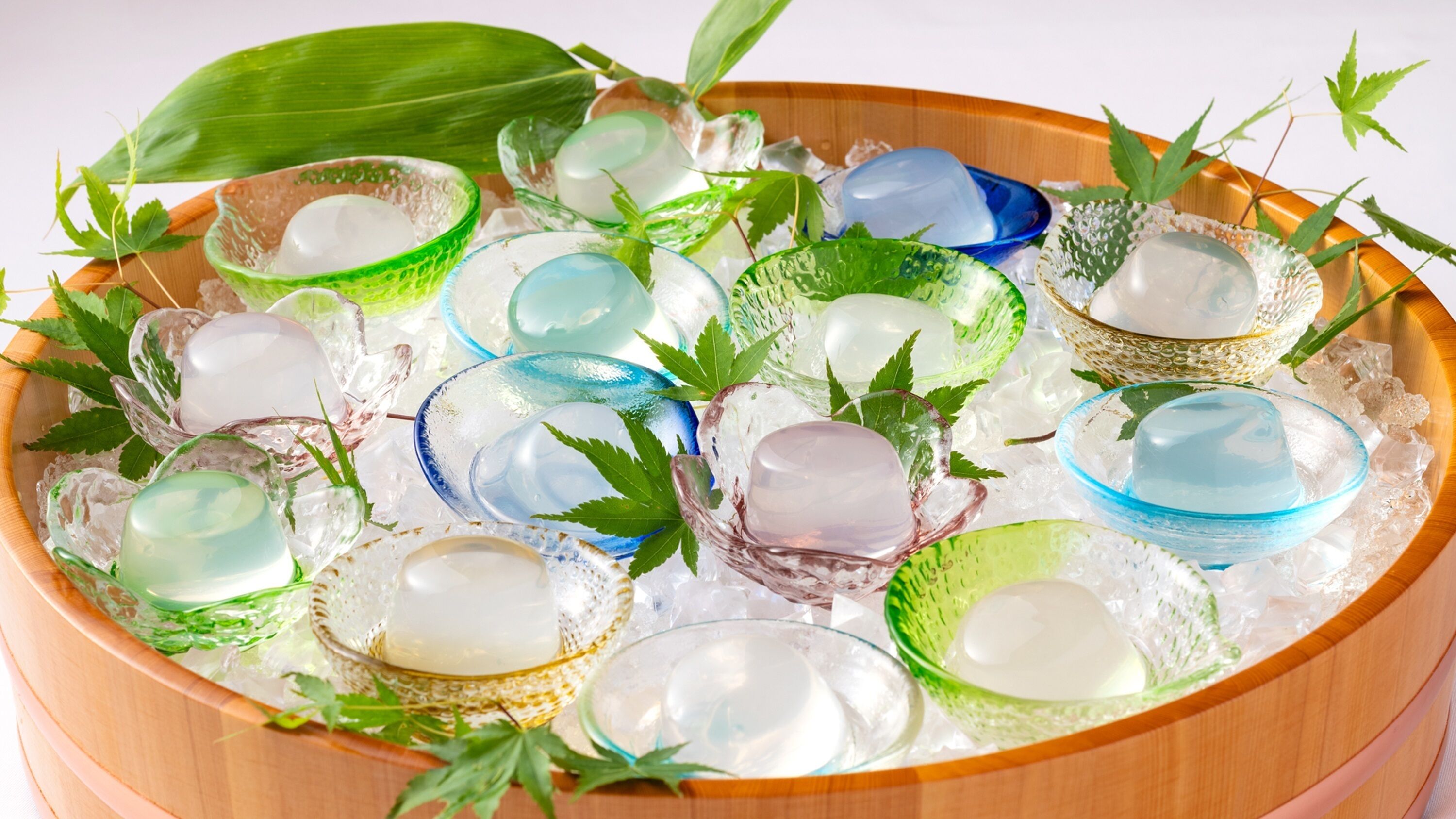A wooden bowl filled with ice and various glass containers, some with green leaves.